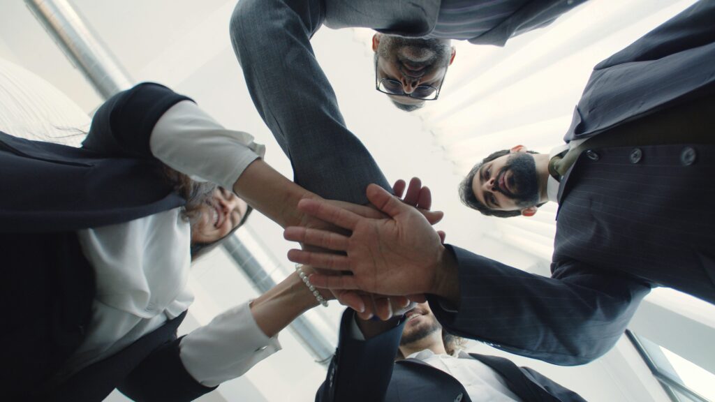 Dynamic low-angle shot of a diverse business team joining hands in unity within a bright, modern office.